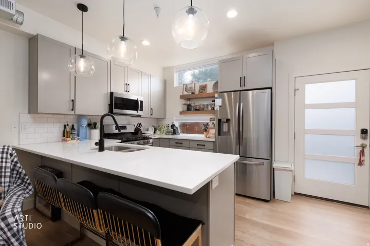 Kitchen featuring light gray cabinetry, white subway tile backsplash, stainless steel appliances, and a central island with a solid surface countertop
