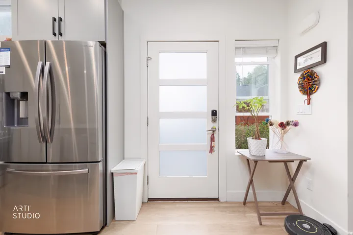 Stainless steel refrigerator, built-in upper cabinetry, wood-finish flooring, smart lock door hardware, and a side window