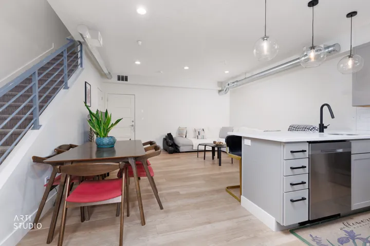 Open-concept living area with wood-finish flooring, a contemporary kitchen island with a built-in dishwasher, and exposed spiral ductwork