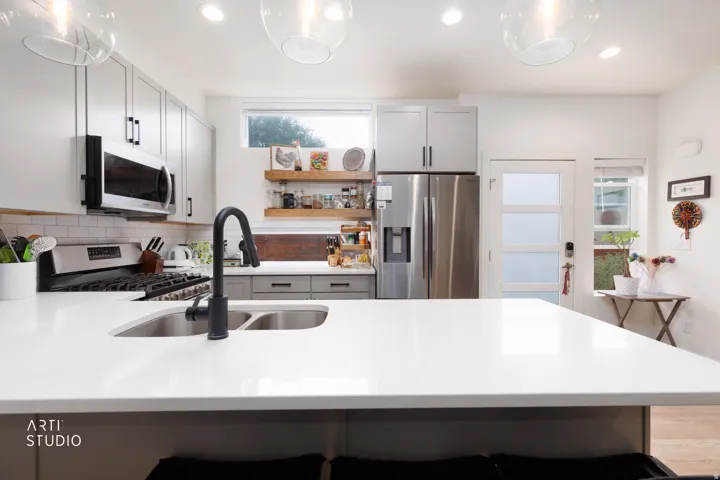 Kitchen featuring a center island with double sink, stainless steel appliances, white cabinetry, and floating wood shelving