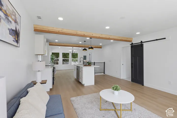 Open-concept living area featuring wood-finish flooring, recessed lighting, exposed ceiling beams, and a modern barn door