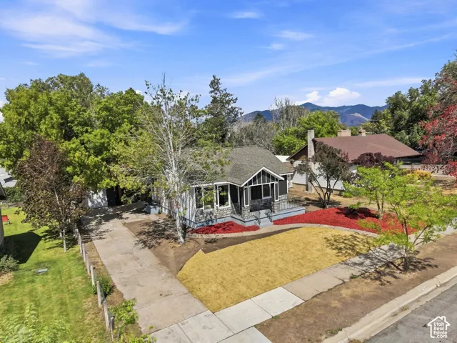 Architectural residence featuring a covered front porch with stone accents, a landscaped front yard with red and yellow ground cover, and a concrete driveway