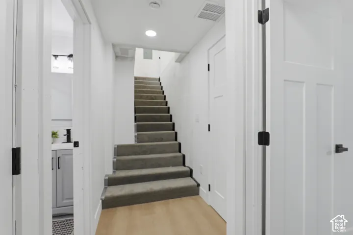 Wood-finish flooring, staircase with carpeted treads, recessed lighting, white panel doors with black hardware, and bathroom vanity with a vessel sink