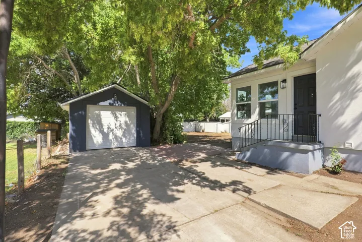 Detached garage, concrete driveway, entry porch with wrought iron railing, exterior sconce, and multi-pane windows