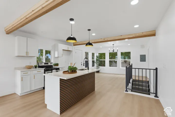 Open-concept kitchen with white cabinetry and gold-finish hardware, central island with seating, recessed lighting, and wood-finish flooring