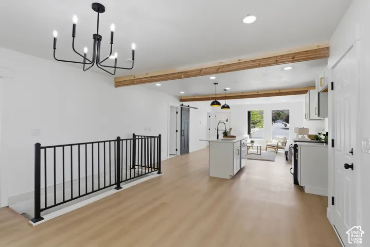 Open-concept living space with light wood-finish flooring, exposed wood beams, and a modern black chandelier