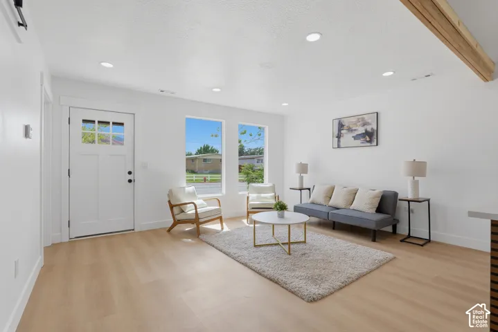 Recessed lighting, wood-finish flooring, white paneled door with glass inserts, exposed wood beam ceiling, and multiple windows