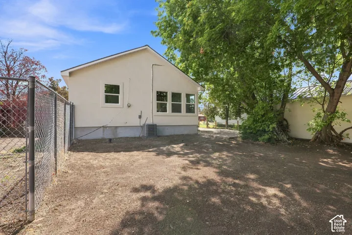 Exterior featuring stucco siding, multiple windows, a chain-link fence, and mature trees