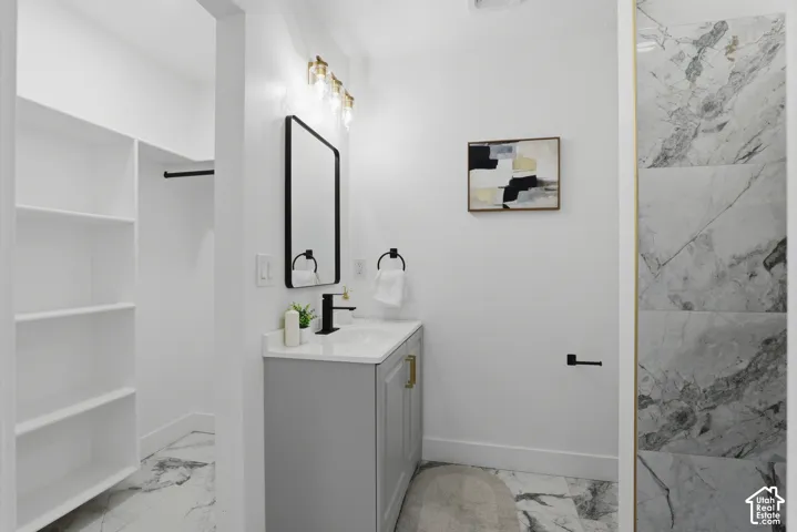 White walls with a light gray vanity and gold-tone hardware, a rectangular mirror, and a wall-mounted light fixture