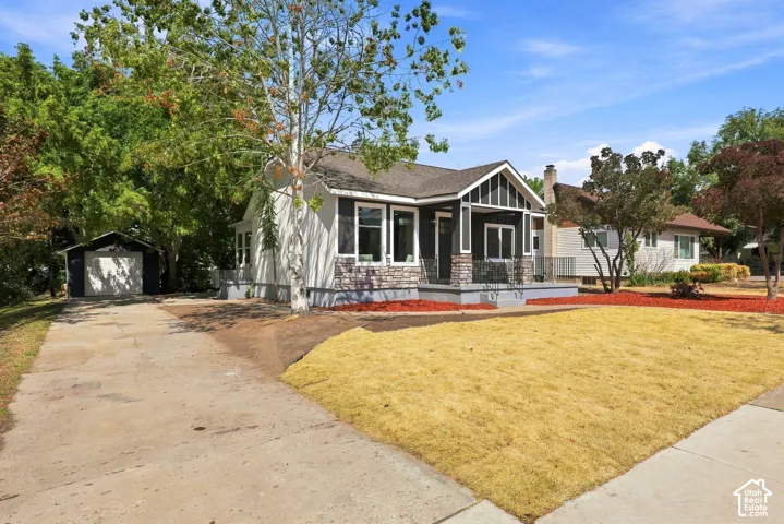 Craftsman-style exterior with stone facade accents, covered front porch, concrete driveway, and detached garage