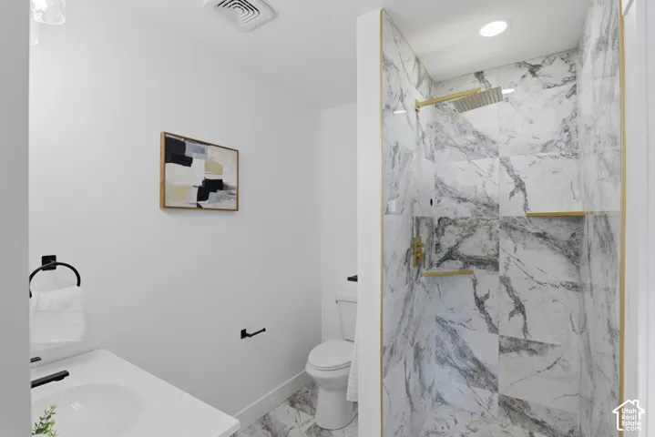 Walk-in shower with full-height marble-finish tile, gold-finish fixtures, and integrated shelving