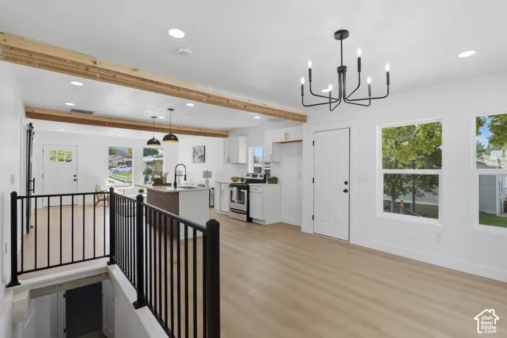 Open-concept living space with exposed wood beams, wood-finish flooring, and a modern black chandelier