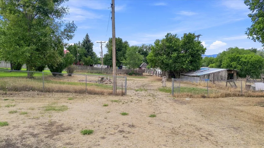 Chain-link fencing with a gate, mature trees, and an outbuilding with a metal roof