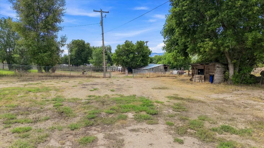 Expansive open lot with mature trees, chain-link fencing, and multiple outbuildings