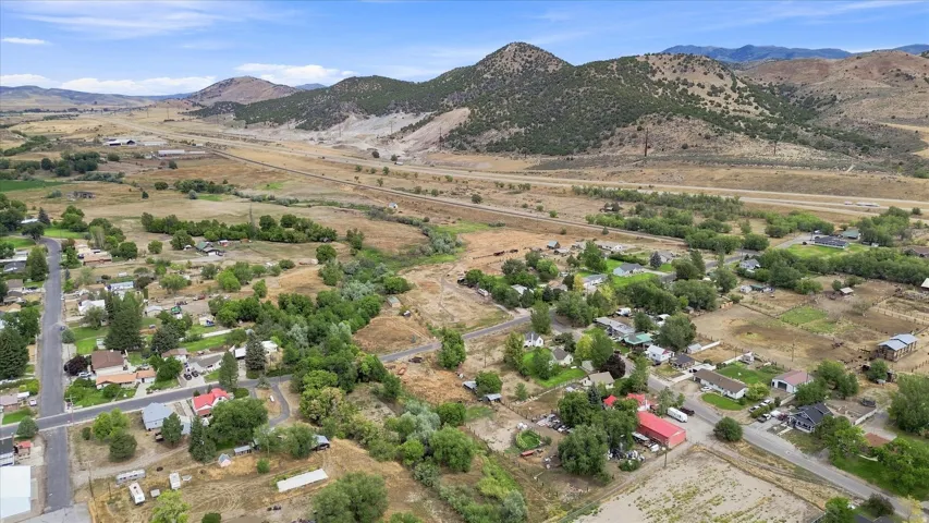 Expansive aerial perspective showcasing a rural landscape with residential properties, mature trees, and mountainous terrain