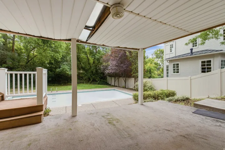 Covered patio with concrete flooring, wood deck with white railings, and an in-ground swimming pool
