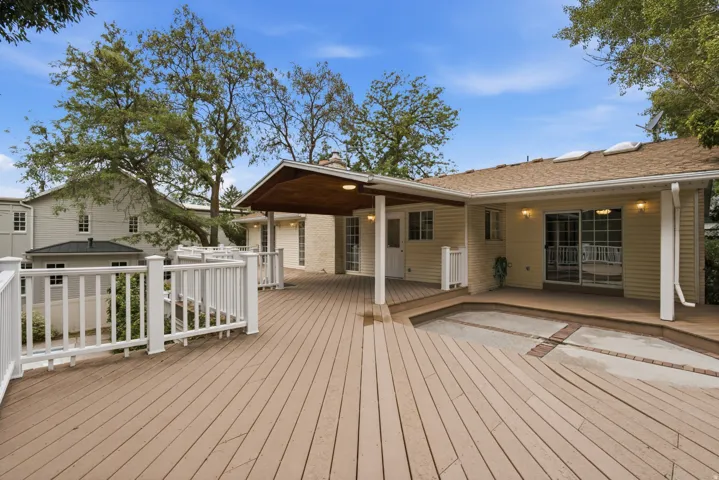 Expansive wood-finish deck with white railings, a covered patio area, and a sliding glass door entry