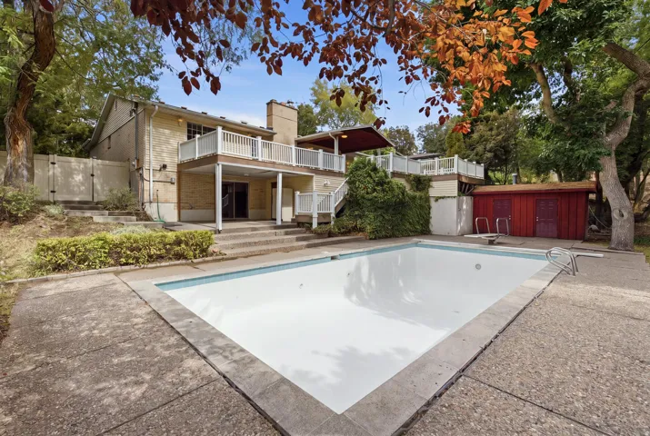 Exterior featuring a multi-level deck with white railings, a ground-level patio, an in-ground swimming pool, and a detached red shed