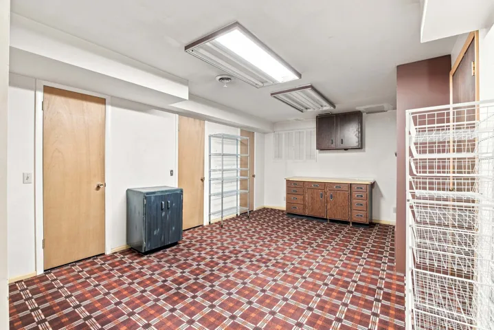 Spacious utility room featuring geometric patterned flooring, recessed ceiling lighting, multiple wood-finish doors with glass panels, built-in cabinetry with drawers and storage, and wall-mounted wire shelving for organized storage solutions