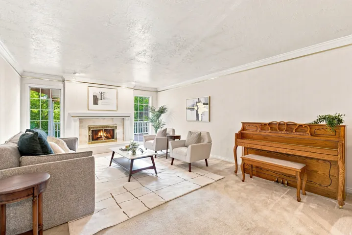 Living area featuring a fireplace with a stone surround, crown molding, and carpet flooring