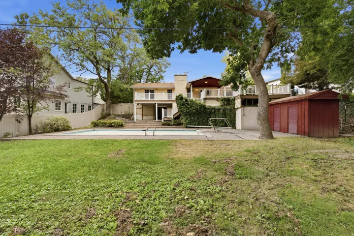 Expansive backyard featuring a swimming pool, multiple outdoor decks, a storage shed, and mature trees