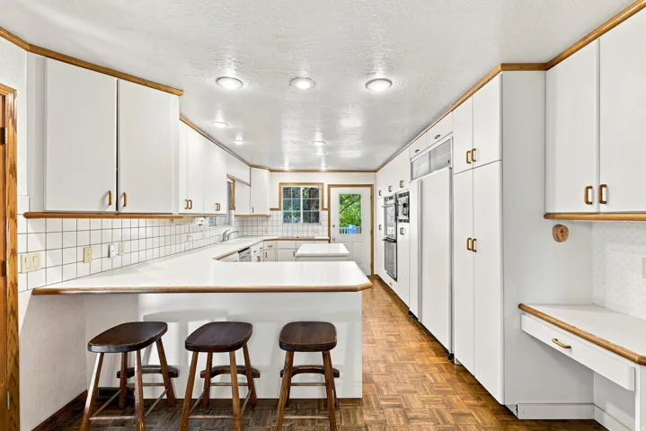 Extensive kitchen featuring white cabinetry with wood trim, white countertops, built-in double ovens, and tile backsplash