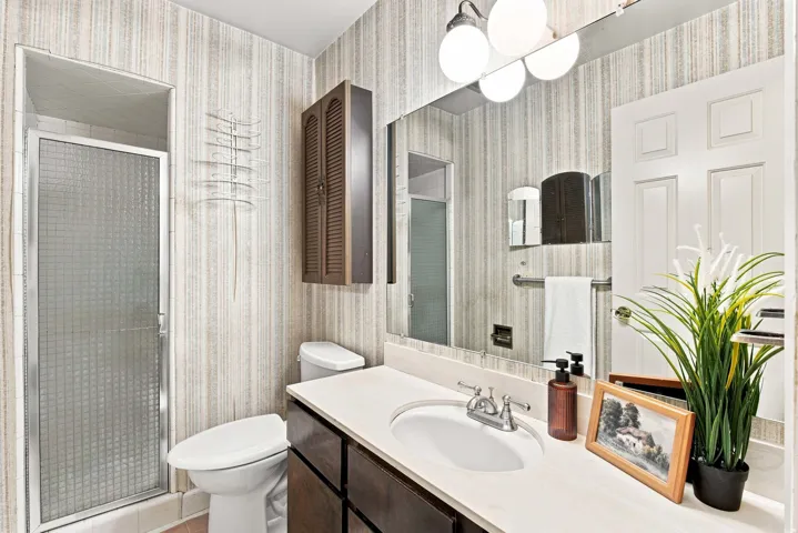 Bathroom featuring a vanity with an integrated sink, a wall-mounted mirror, a shower with a textured glass door, and a built-in wall cabinet