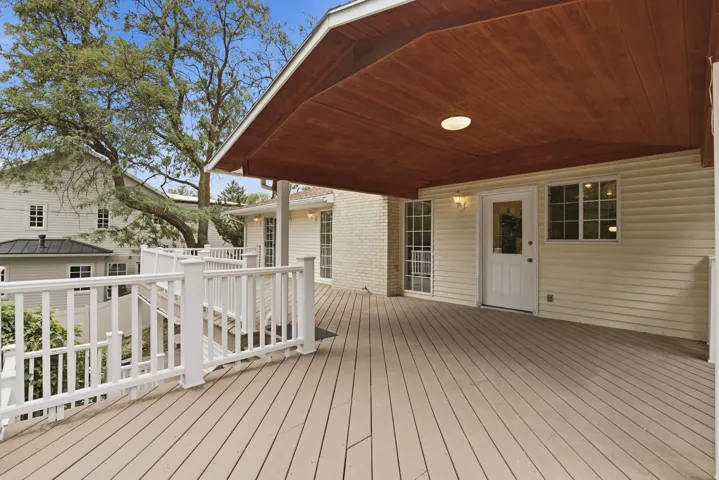 Expansive outdoor deck with composite decking, white railing, and a rich wood-finish ceiling with recessed lighting