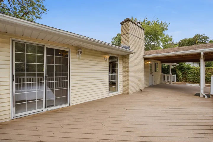 Expansive wood-finish deck with a covered patio area, brick chimney, and sliding glass door access