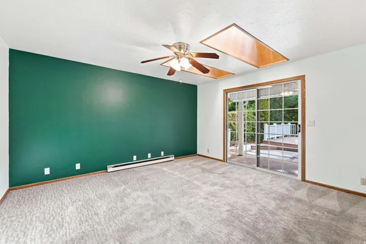 Carpeted room with a ceiling fan, dual skylights, and sliding glass doors leading to an exterior deck