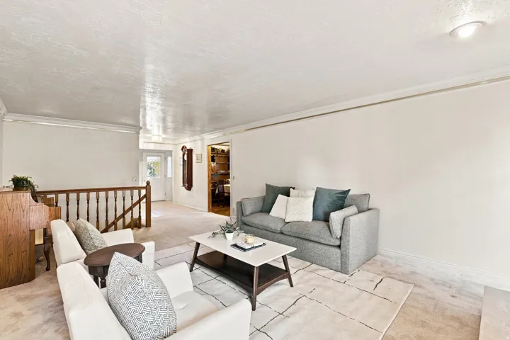 Carpeted living area with crown molding, recessed lighting, and a wood-finish staircase railing