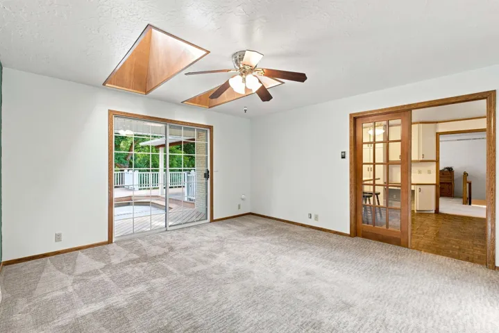 Recessed skylight, ceiling fan, sliding glass door, wood-frame glass panel pocket door, and light gray patterned carpeting