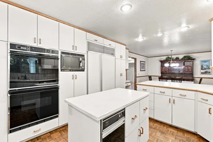 Kitchen featuring white cabinetry, built-in double ovens, built-in microwave, a central island, and wood-finish flooring