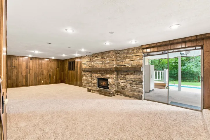 Wood-paneled accent wall, stone-front fireplace with a wood mantel, recessed ceiling lighting, sliding glass door, and outdoor patio access