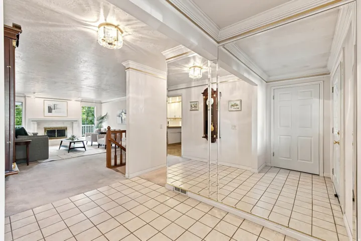 Tiled entry flooring, paneled front door, crown molding, and a visible living area with a fireplace