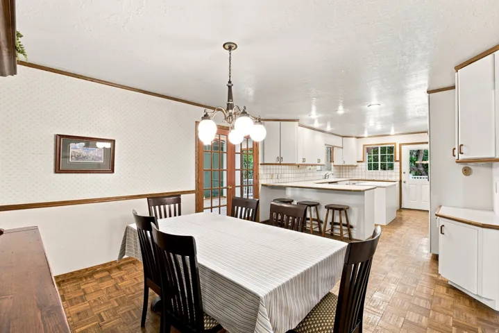 Kitchen and dining area featuring parquet wood-finish flooring, white cabinetry, a tiled backsplash, and recessed lighting