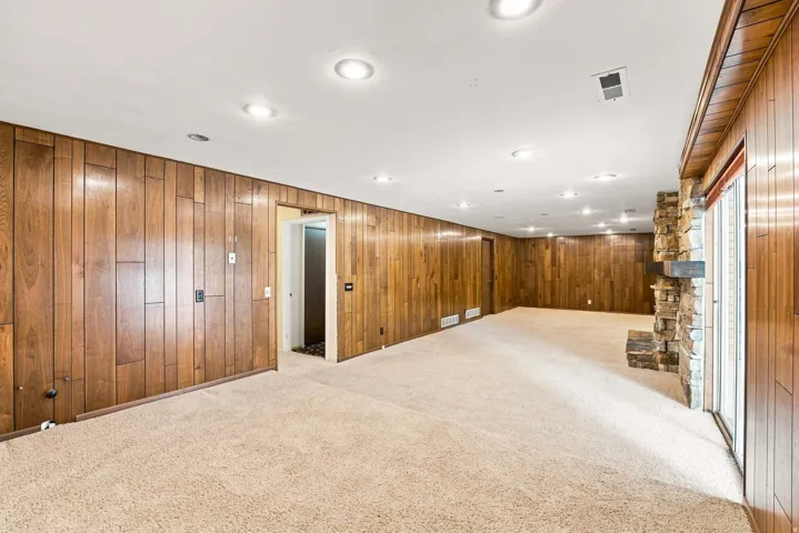 Expansive carpeted room featuring extensive wood paneling and recessed lighting