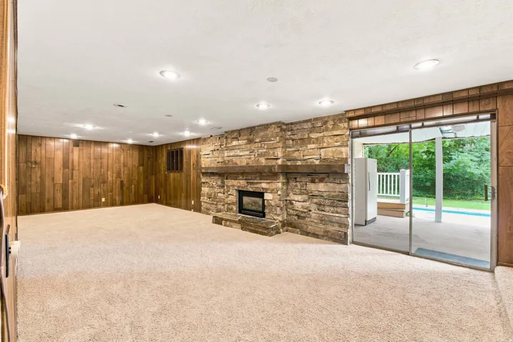 Stone-finish fireplace with hearth, wood-paneled walls, recessed lighting, and sliding glass door