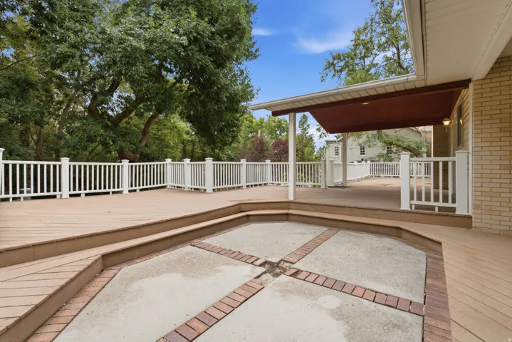 Multi-level deck with white railings, featuring a covered patio area and a lower-level paver patio