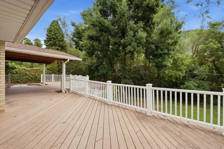 Expansive wood-finish deck with white railings, featuring a covered patio area and brick exterior accents