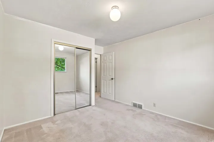 Carpeted flooring, mirrored sliding closet doors, window with natural light, and a white interior door