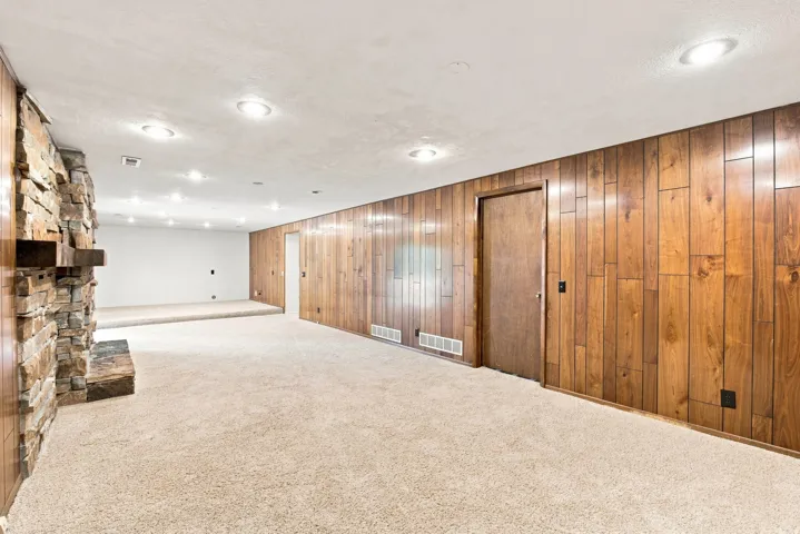 Stone-clad fireplace, wood paneling, recessed lighting, and soft carpet flooring