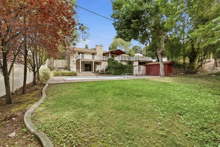 Expansive lawn area, rectangular swimming pool, multi-level decking, white perimeter fencing, and mature trees