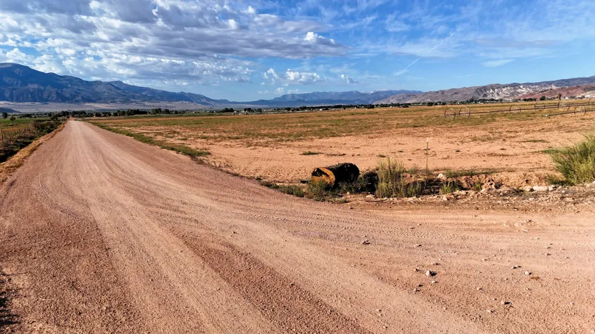 Expansive rural property featuring an unpaved road, arid terrain, and distant mountains under a cloudy sky