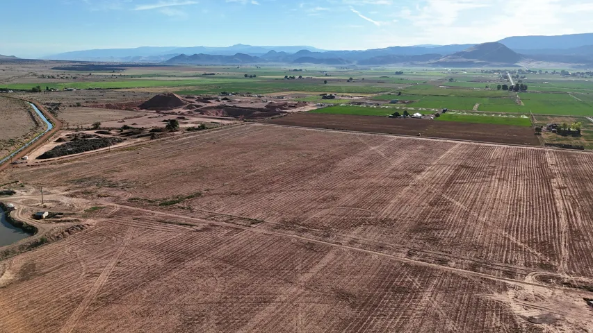 Expansive land featuring tilled fields, a visible irrigation canal, and distant mountains