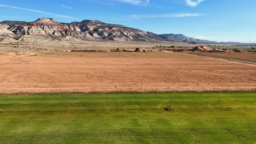 Expansive land featuring a large green field, brown cultivated terrain, and distant mountains under a clear sky