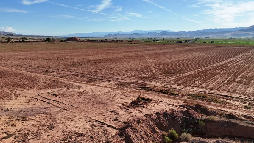Expansive cleared land with visible soil preparation, set against a backdrop of distant mountains