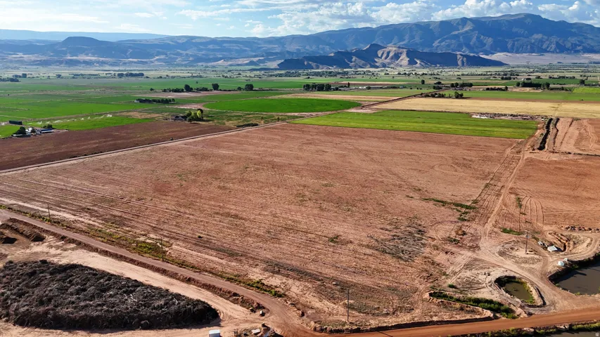 Expansive land parcel featuring open fields, distant mountains, and established roads