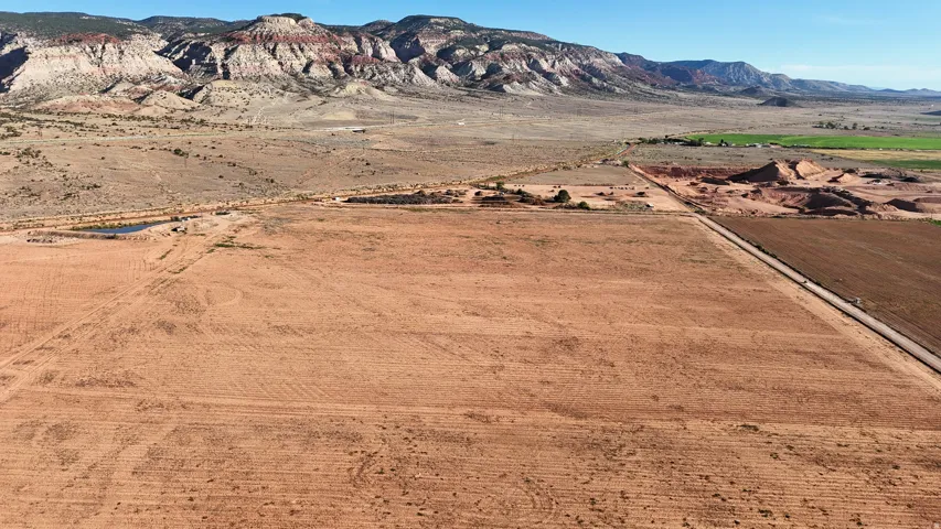 Expansive open land with distant mountain ranges, a water retention pond, and a defined roadway