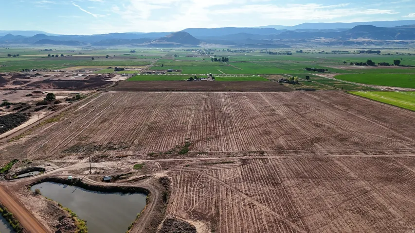Expansive agricultural land featuring a tilled field, a water retention pond, and distant green pastures